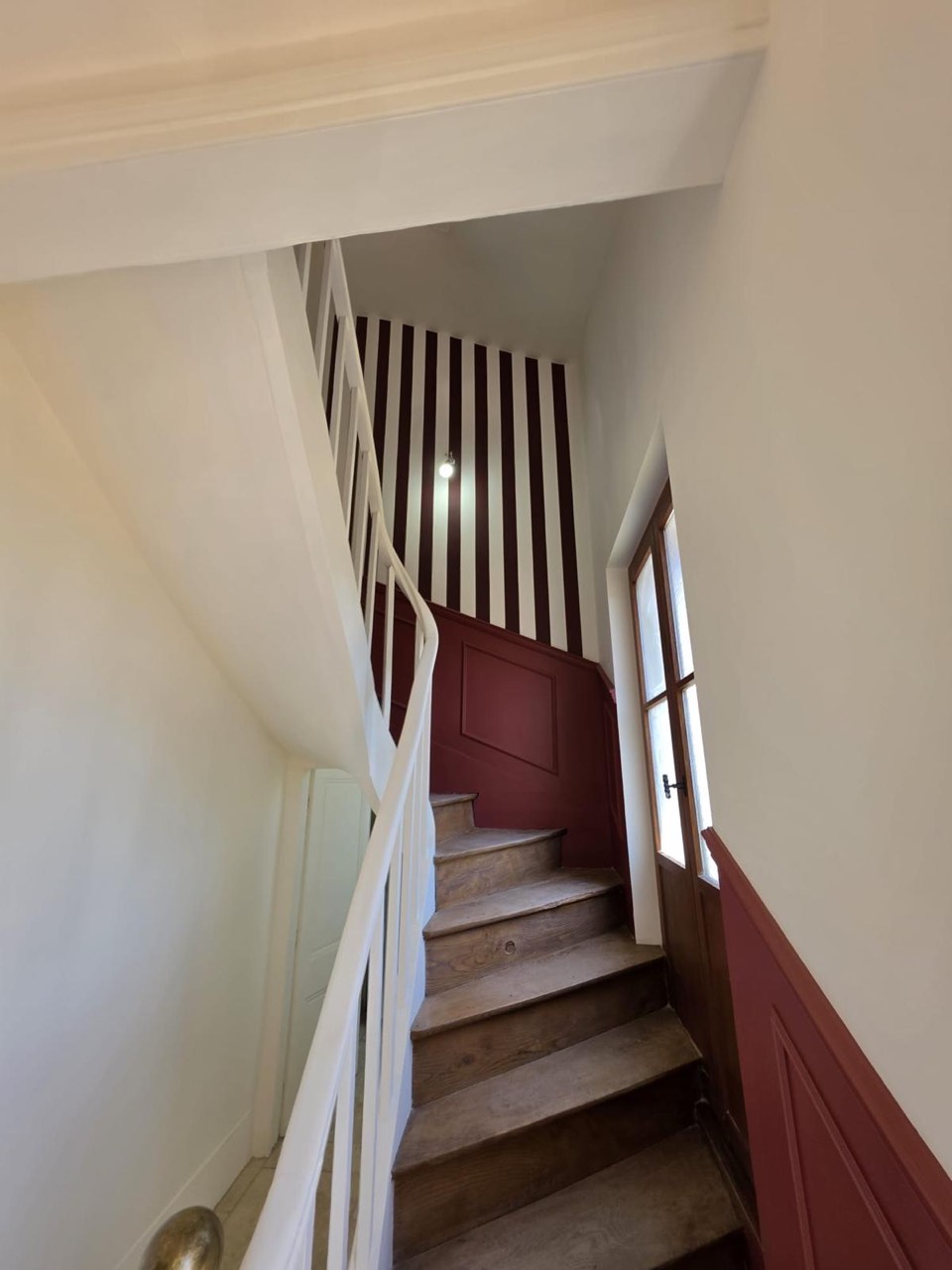 Cage d'escalier rénovée en peinture : soubassement et rayures bordeaux, murs blancs, marches bois et rampe blanche — chantier à Pont-Audemer