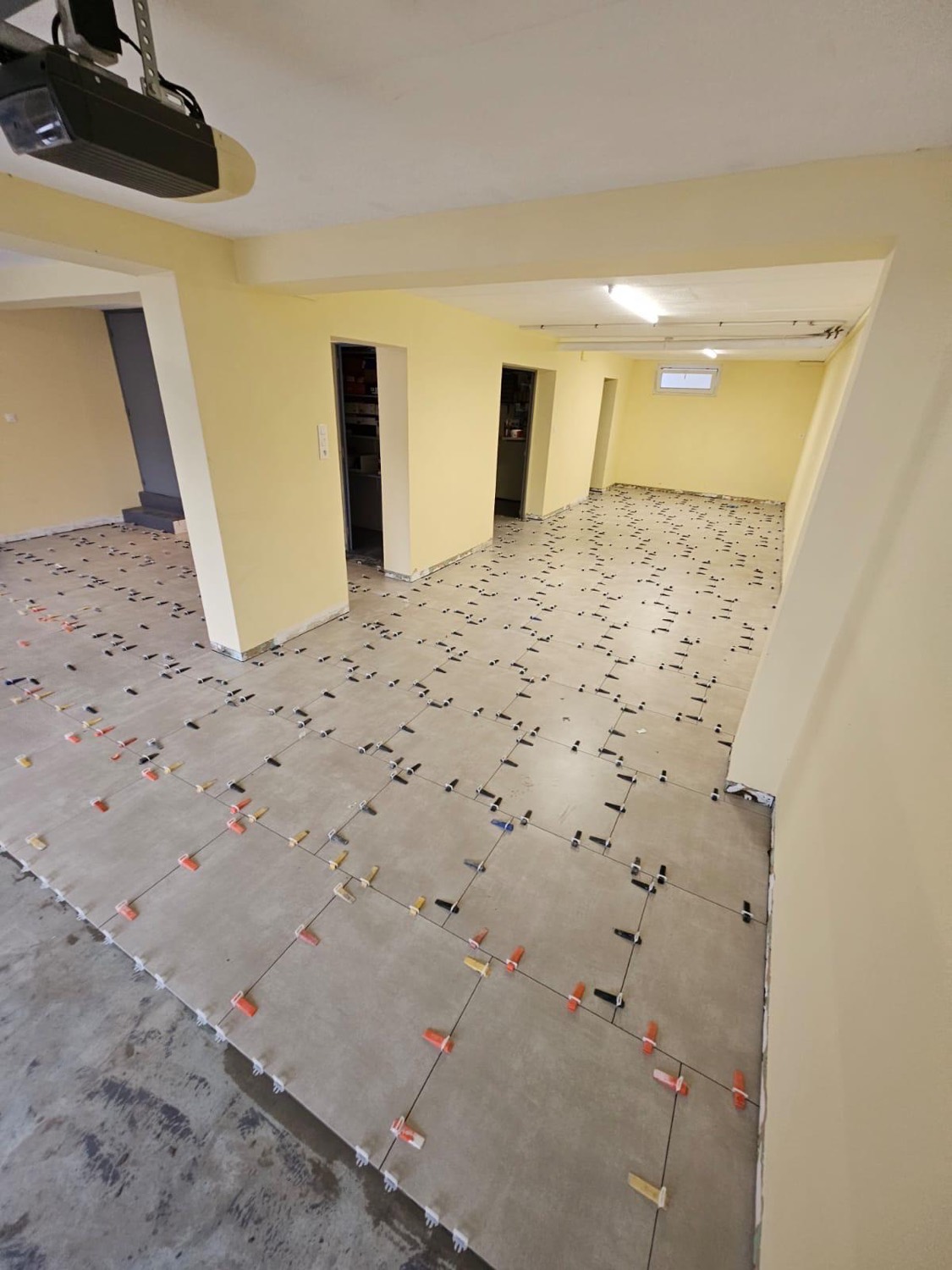 Pose de carrelage grand format au sol d'un garage, avec croisillons de nivellement — chantier à Équemauville