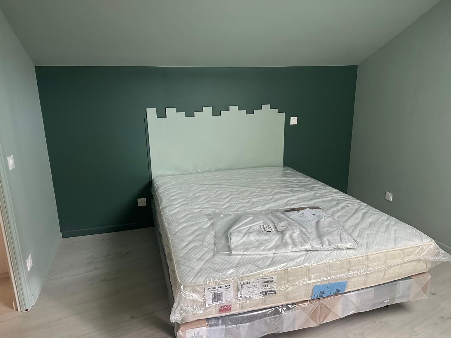 Chambre en cours d'aménagement, tête de lit peinte et sol stratifié clair