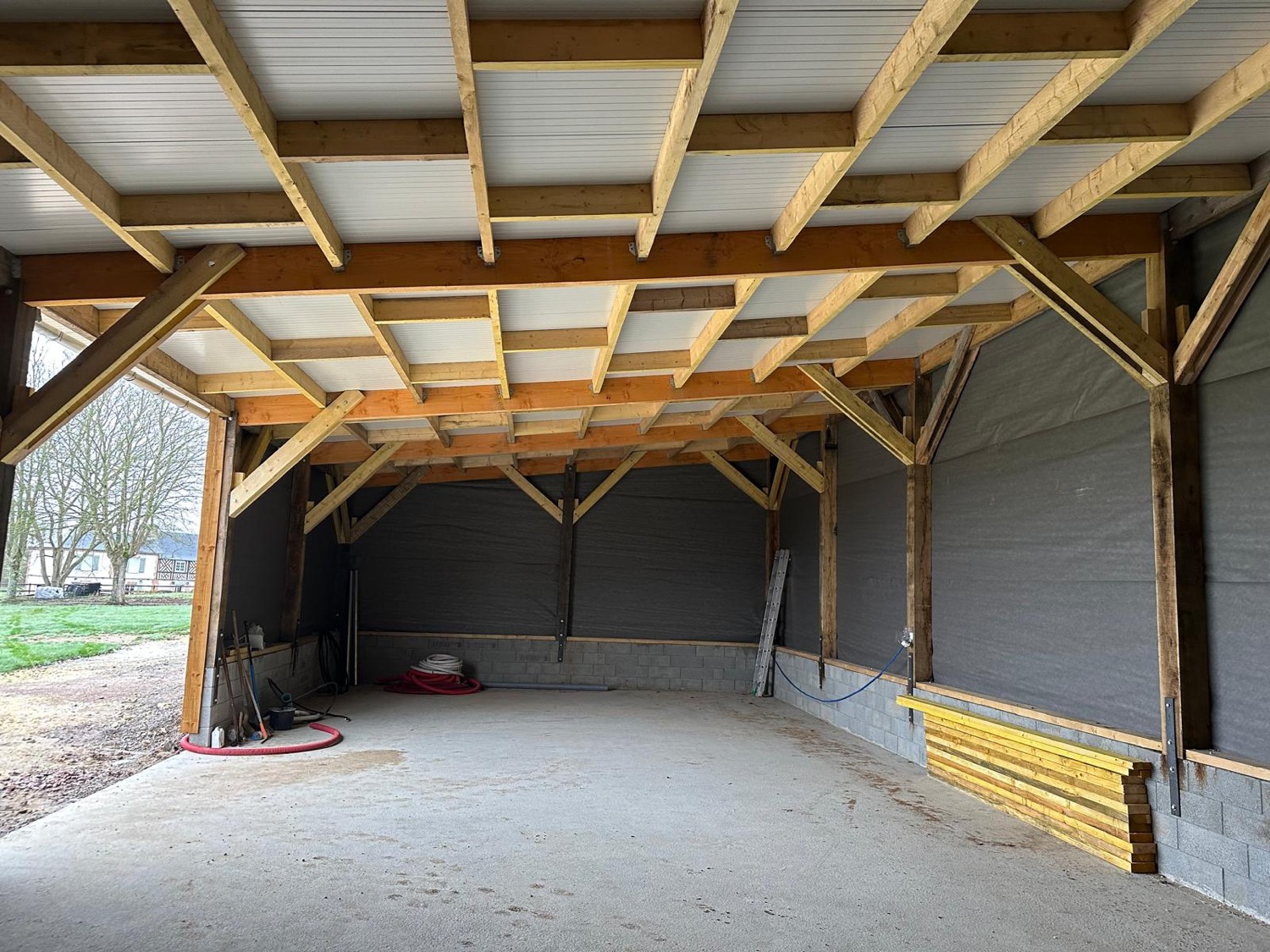 Intérieur de l'écurie : charpente bois apparente, ouvert sur la campagne normande