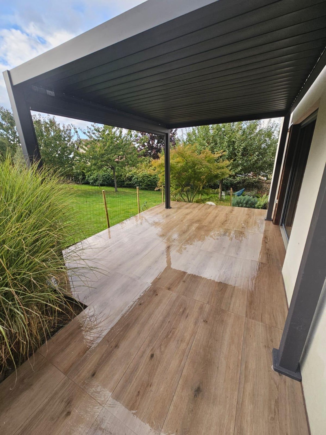 Terrasse abritée par la pergola bioclimatique, ouverte sur le jardin