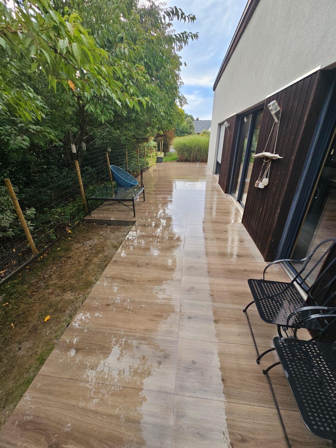 Terrasse périphérique en carrelage imitation bois longeant la façade à bardage