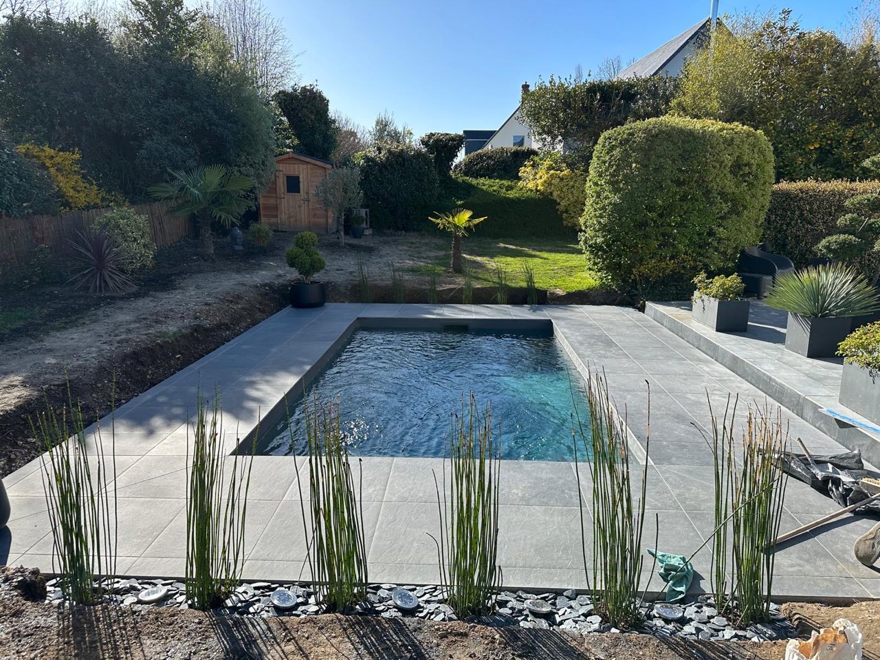 Piscine extérieure rectangulaire avec plage en carrelage gris grand format, entourée d'un jardin paysager — chantier à Saint-Gatien-des-Bois