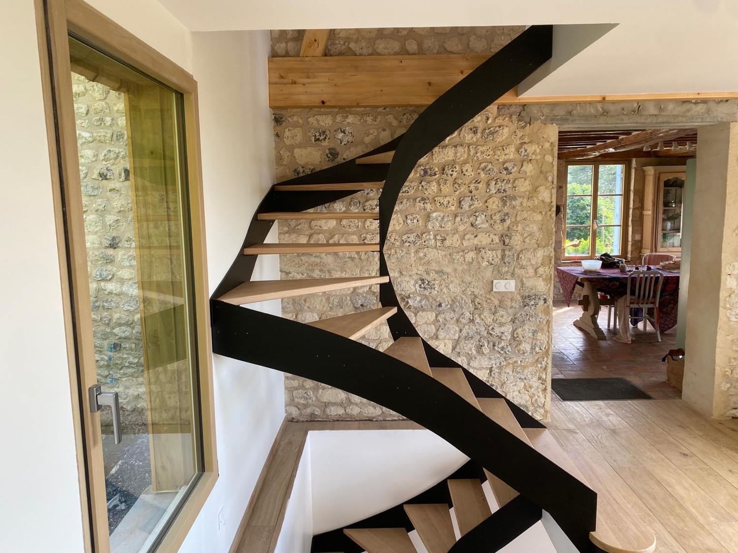 Escalier sur mesure à limon métal noir et marches en chêne contre un mur en pierre, dans une maison rénovée au Havre