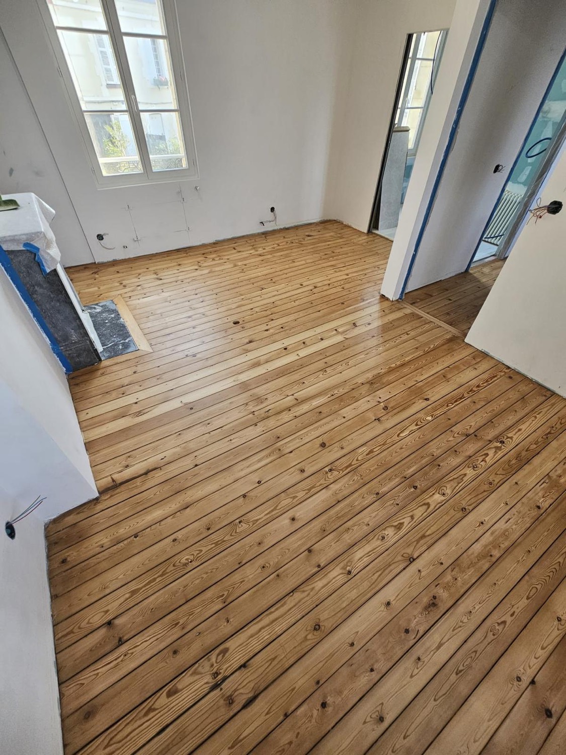 Parquet en pin poncé et vitrifié après rénovation, murs fraîchement repeints en blanc — chantier à Pont-l'Évêque