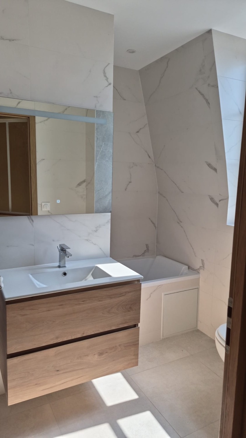 Salle de bain sous combles avec baignoire, meuble vasque bois et faïence effet marbre
