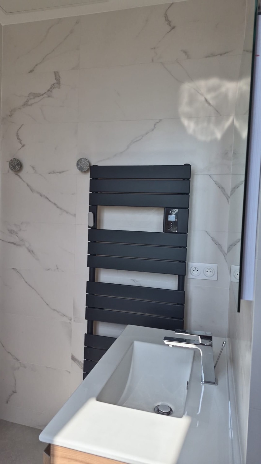 Salle de bain en faïence marbre blanc avec sèche-serviettes noir et meuble vasque bois
