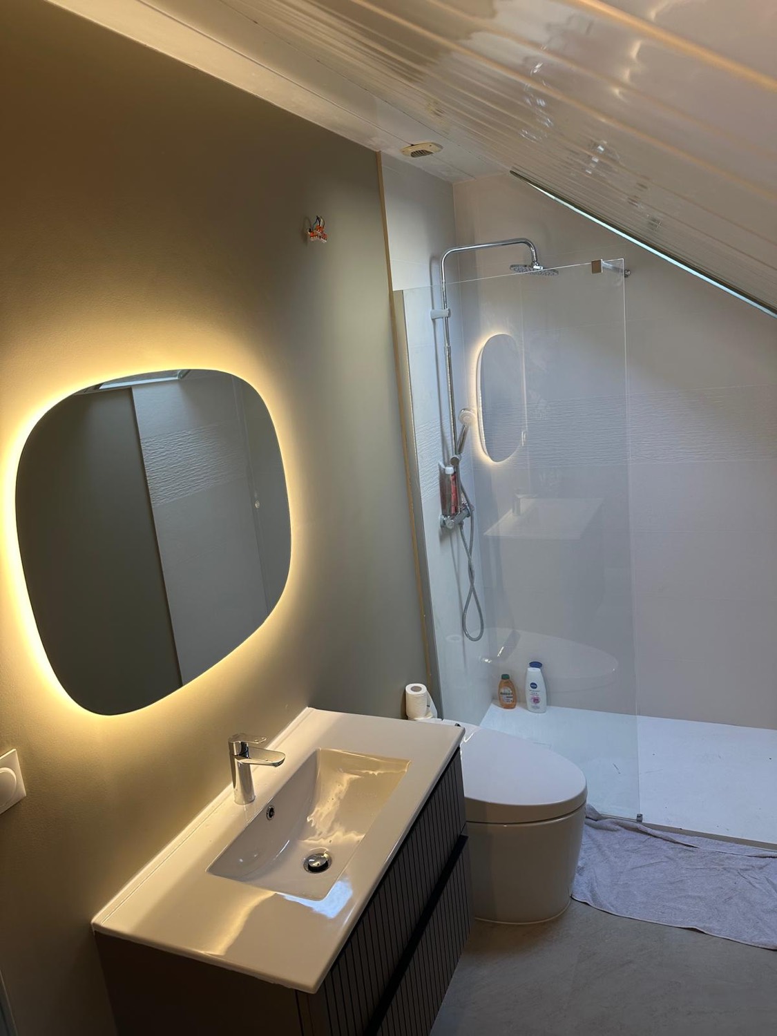 Salle de bain sous combles avec éclairage d'ambiance, faïence texturée et fenêtre de toit