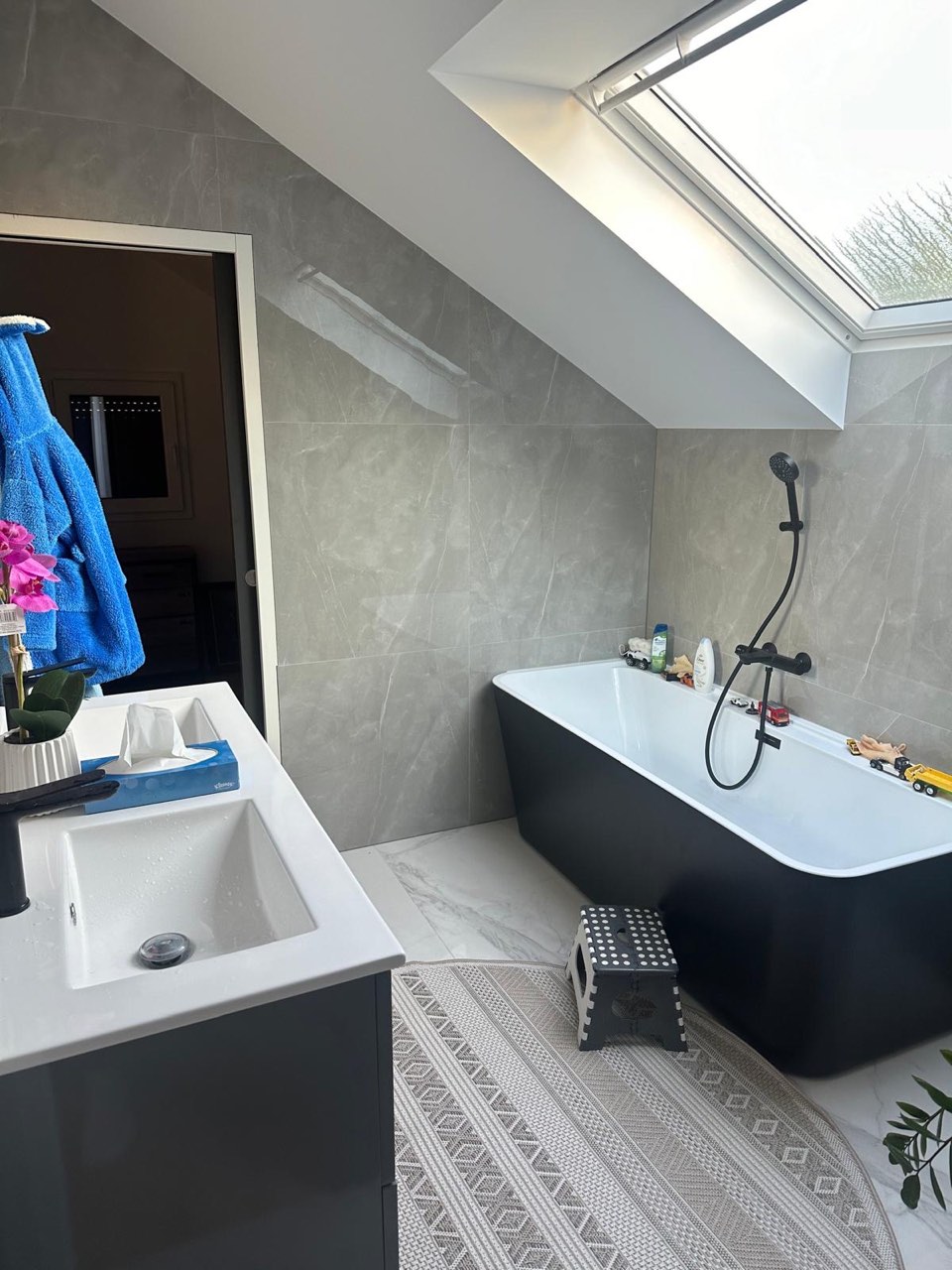 Baignoire îlot noire et meuble vasque dans une salle de bain sous combles à Lisieux, faïence marbre gris