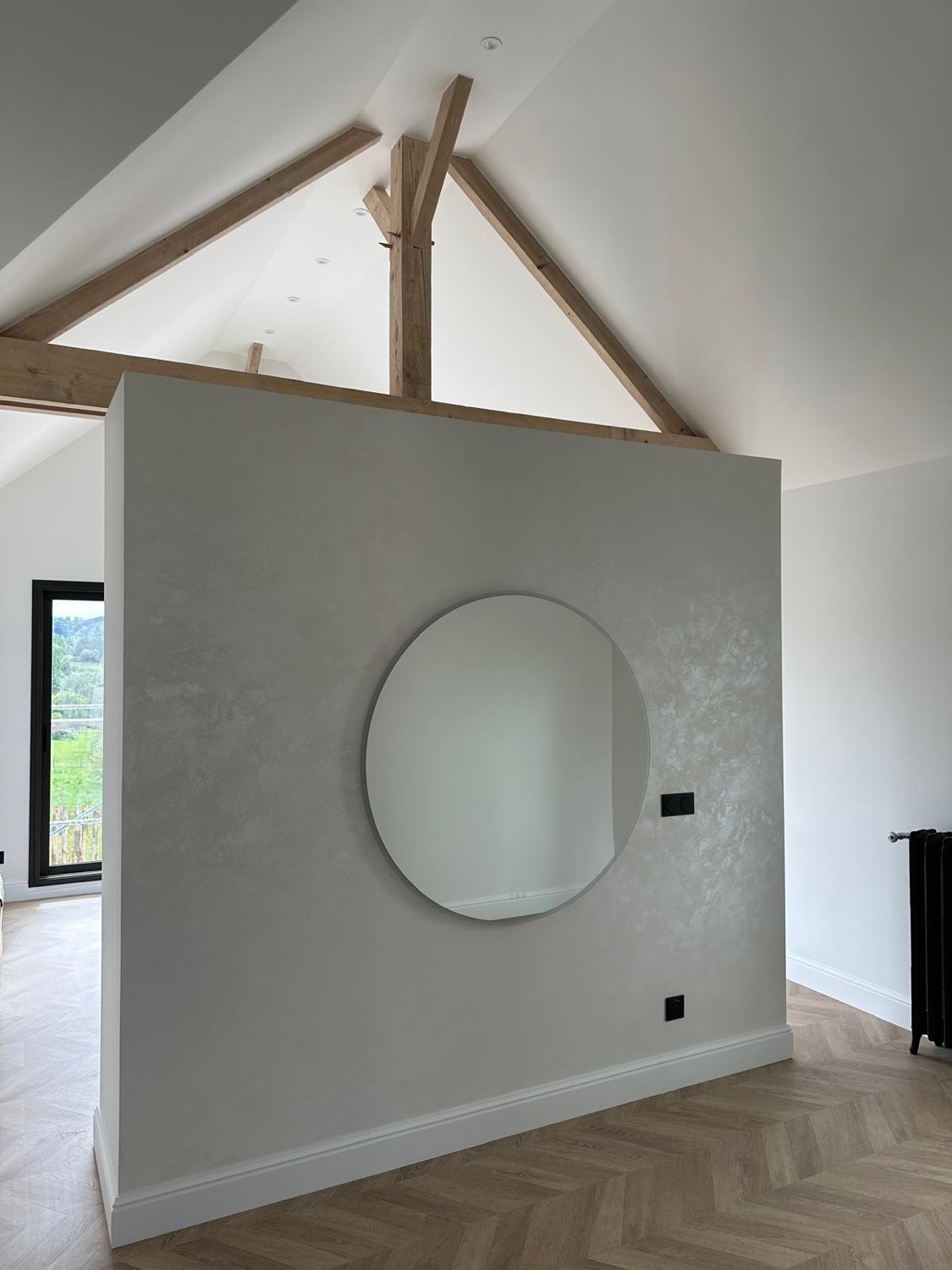 Chambre avec mur en béton ciré gris, miroir rond et charpente bois apparente