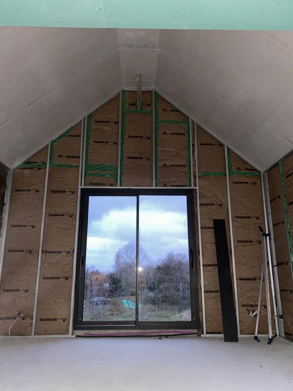 Pièce en chantier avec isolation, ossature et baie vitrée posée sous plafond cathédrale