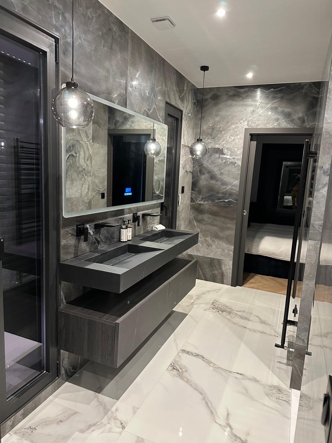 Salle de bain en marbre anthracite avec double vasque suspendue, douche à l'italienne et vue sur la chambre — chantier à Pennedepie