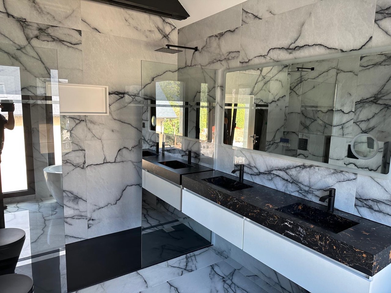 Salle de bain entièrement habillée de marbre veiné avec double vasque noire, douche à l'italienne et baignoire îlot