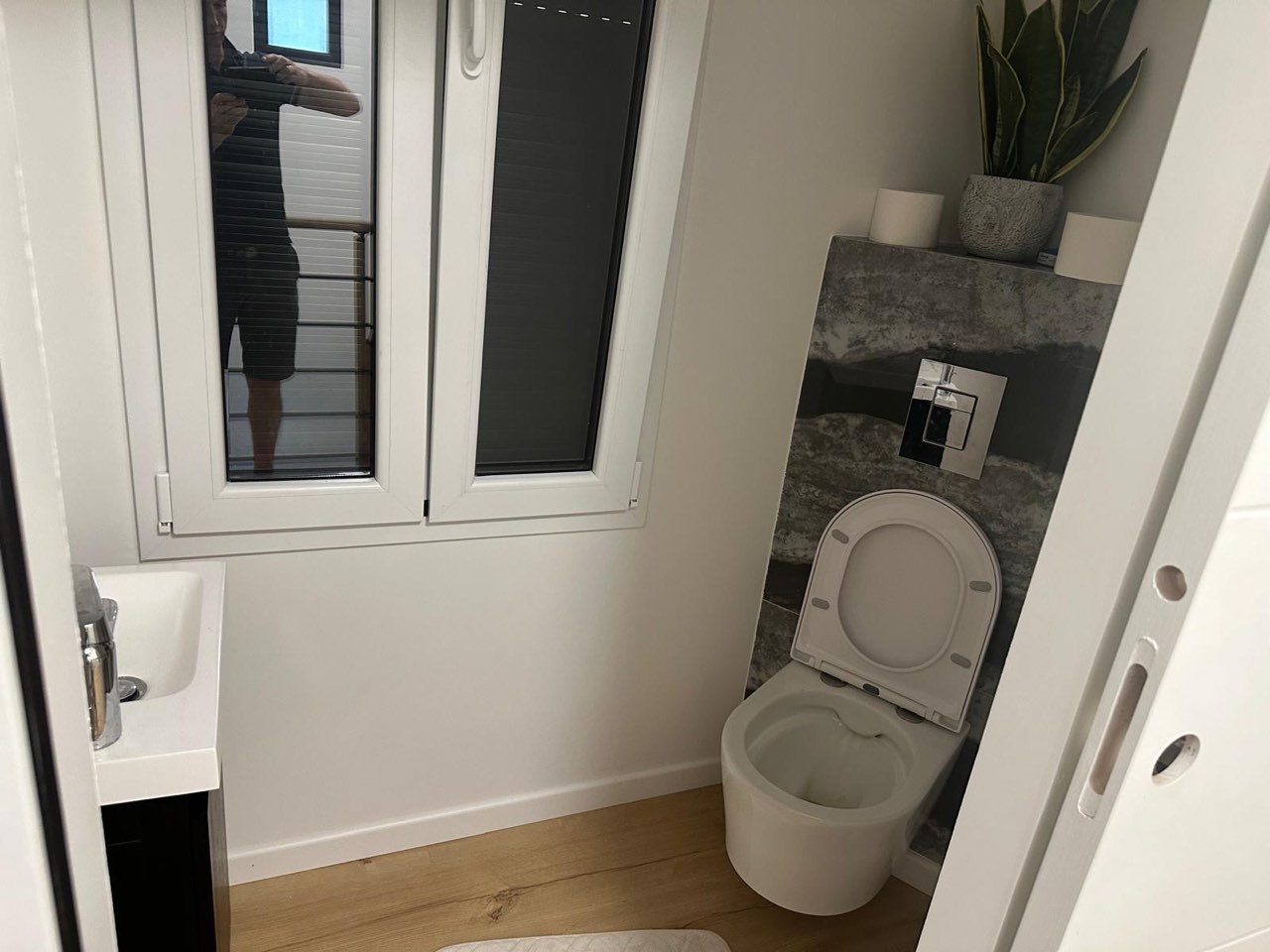 WC suspendu avec crédence en pierre grise, lave-mains et sol en parquet, fenêtre apportant la lumière — chantier à Beaumont-en-Auge